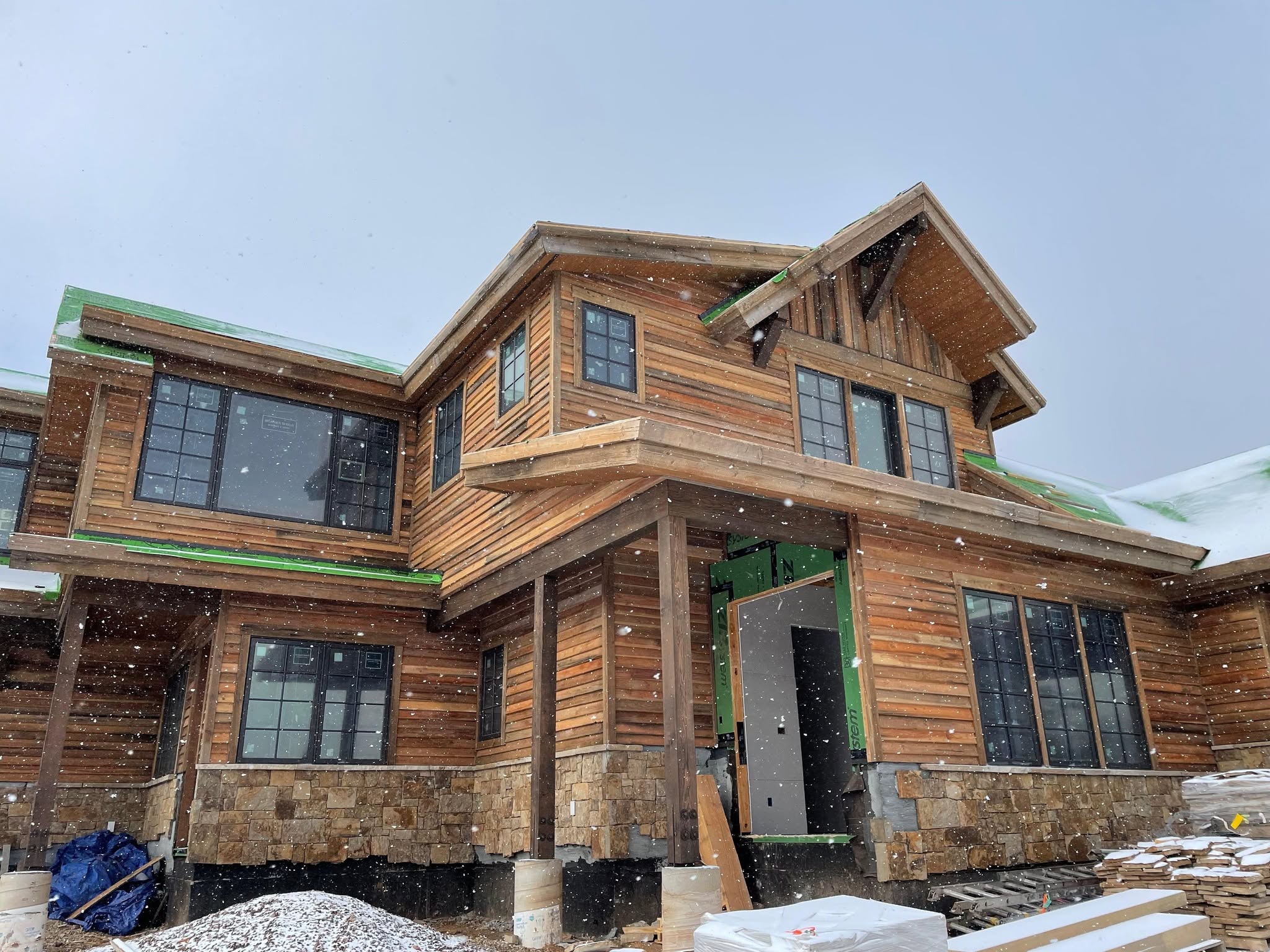 Snow falling around a cedar and stone mountain home under construction